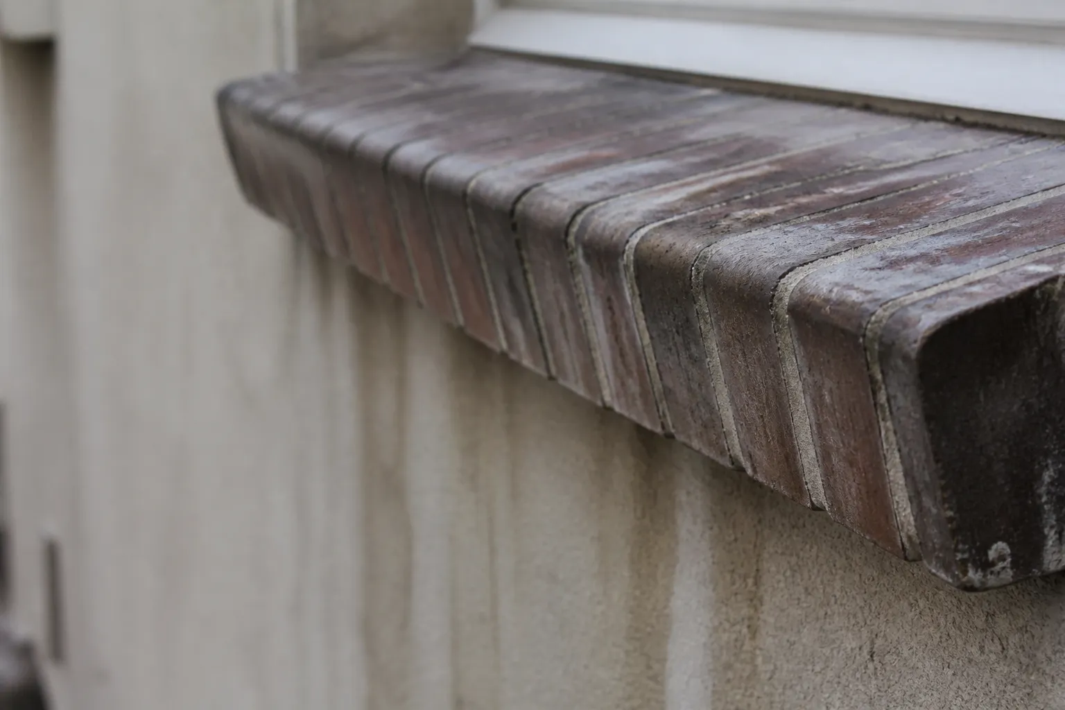 Appui de fenêtre ancien en briques posées sur chant, vu de biais depuis l’extérieur : léger débord, pente d’écoulement, rejingot en relief et traces de ruissellement