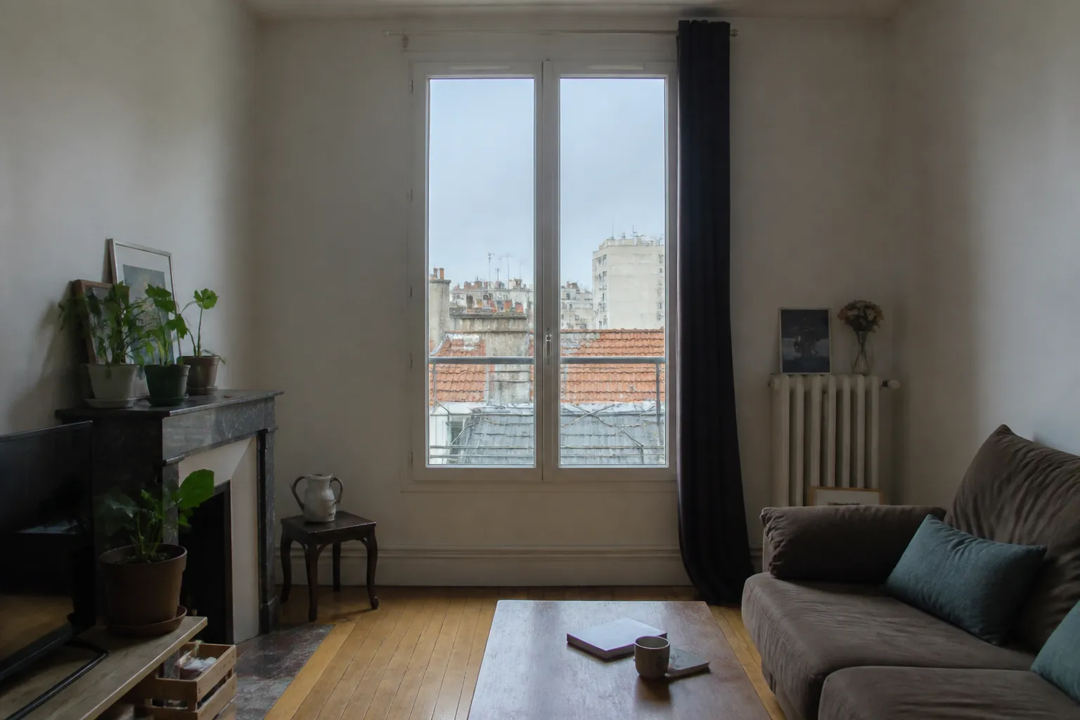 Séjour d’appartement ancien rénové et habité : fenêtre neuve à deux vantaux au centre du cadre, parquet remis en état, mobilier ordinaire, lumière froide d’un jour couvert