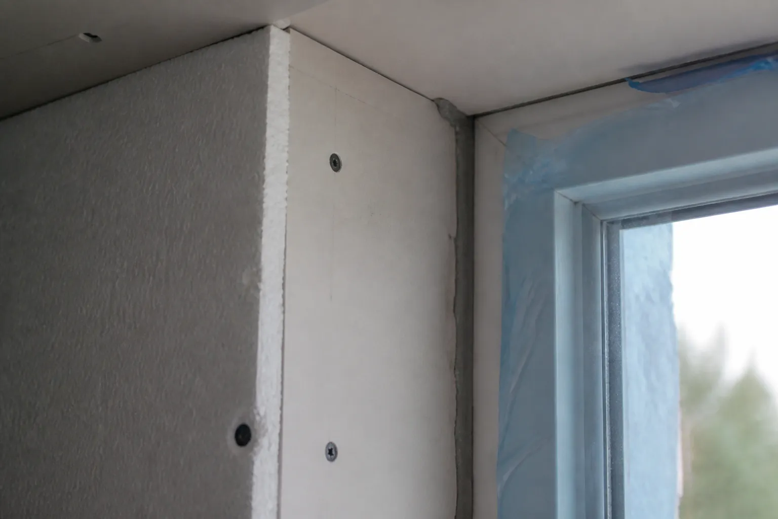 Angle intérieur d’une baie en finition : le doublage isolant revient en tableau contre le dormant de la menuiserie neuve, joint de calfeutrement souple appliqué à la jonction