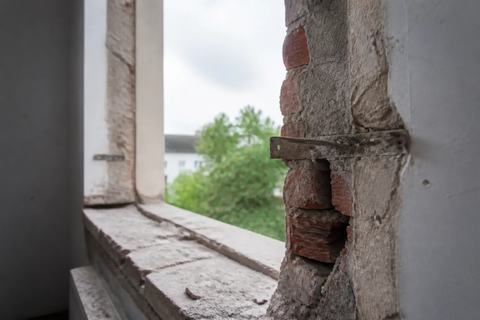 Tableau de baie entièrement mis à nu après dépose de la menuiserie : jambages de brique et d’enduit ancien, pattes de scellement encore fichées dans le mur, appui en attente